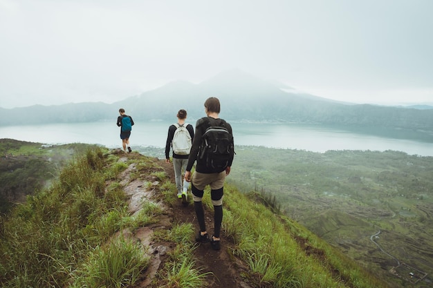 3 men walk along hill with backpacks with white clouds peak volcano background_501050 2